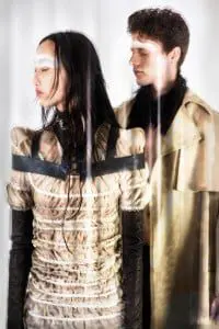 Je t'aime Taner Tumkaya: Mark wears tan coat and black trousers by Harold Kensington, jacket by Nine Muses. Anita wears tan knitted bell bottoms by Maria Dora, shear pucker dress by Genevieve Clifford, black neck panel and dark brown glove by Mother of London