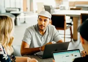 A group of professionals gathered around a table with laptops in an office space, discussing organizational knowledge and its role in gaining a competitive advantage