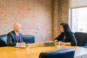 Two professionals sitting at a table in a conference room with a laptop, discussing organizational knowledge and its significance